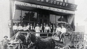A faded black and white photo of many people standing in front of a horse buggy