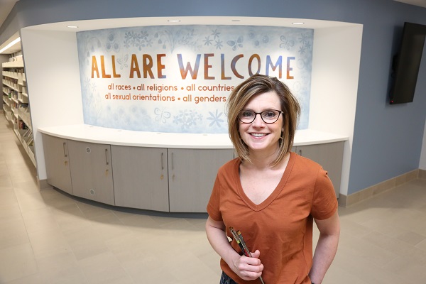 Artist Bonnie Lecat stands in front of the library's All Are Welcome mural