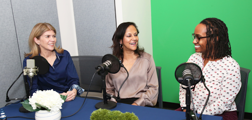 Three women sitting at a table in front of podcast microphones