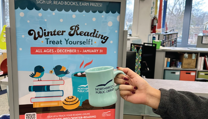 A photo of the Winter Reading sign with a mug being held in front of it