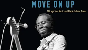 A photo of a black male musician playing the guitar on stage